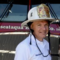 Assistant Fire Chief Don Matheson in front of a fire truck wearing a white Assistant Chief Helmet