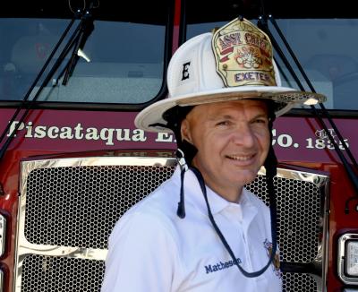 Assistant Fire Chief Don Matheson in front of a fire truck wearing a white Assistant Chief Helmet