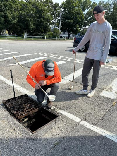 people testing water in a drain for mosquitos